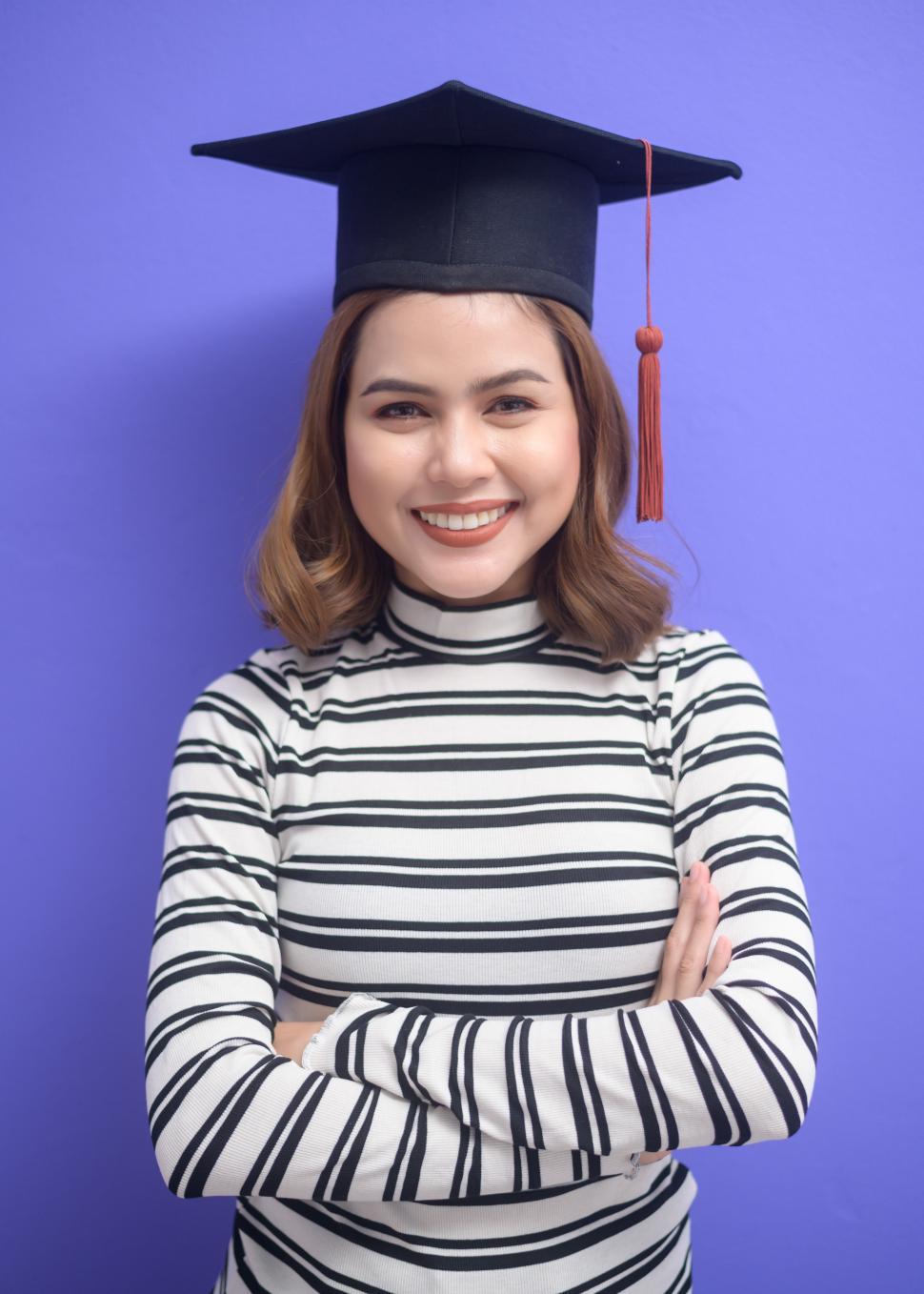 Free Image of Portrait of young woman graduate with arms crossed over purple background 