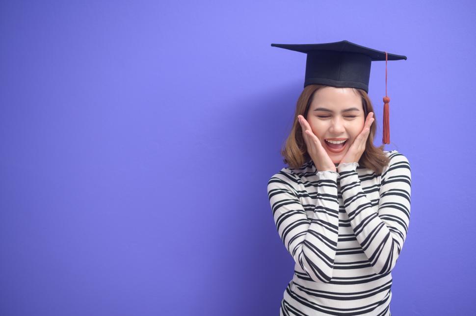 Free Image of Young graduate exclaims with hands on cheeks over colorful background 