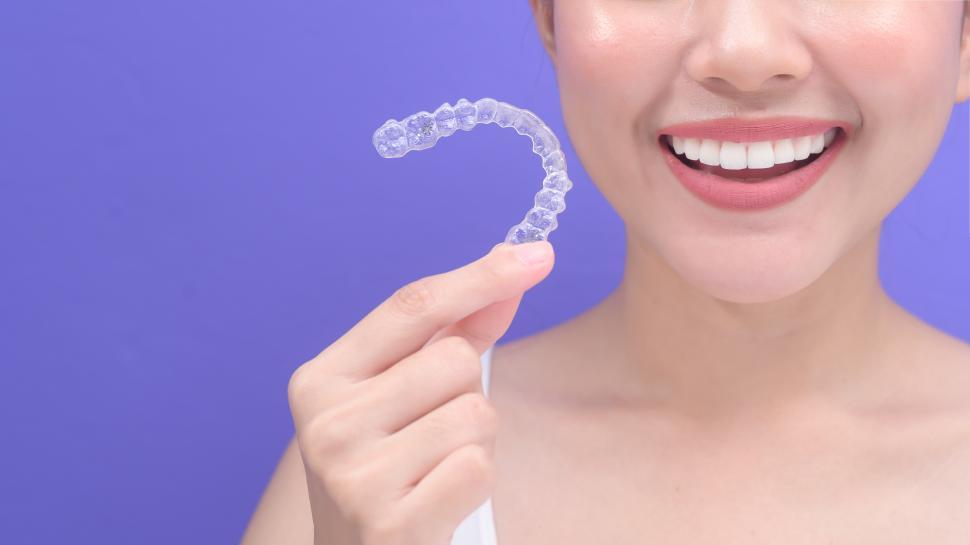 Free Image of Young smiling woman holding invisible plastic braces tray in studio, dental concept 