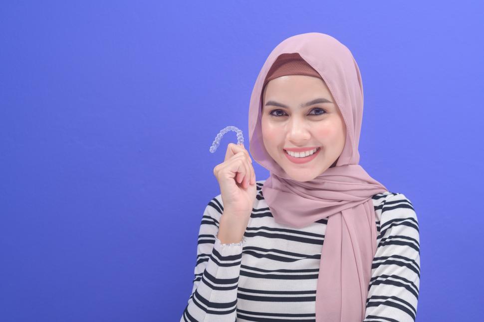 Free Image of Young muslim woman holding invisible plastic braces in studio, dental hygene 