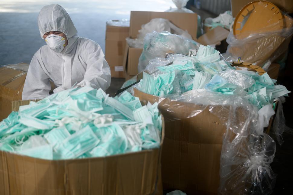 Free Image of Bins of used medical masks in waste recycling facility with worker in PPE 