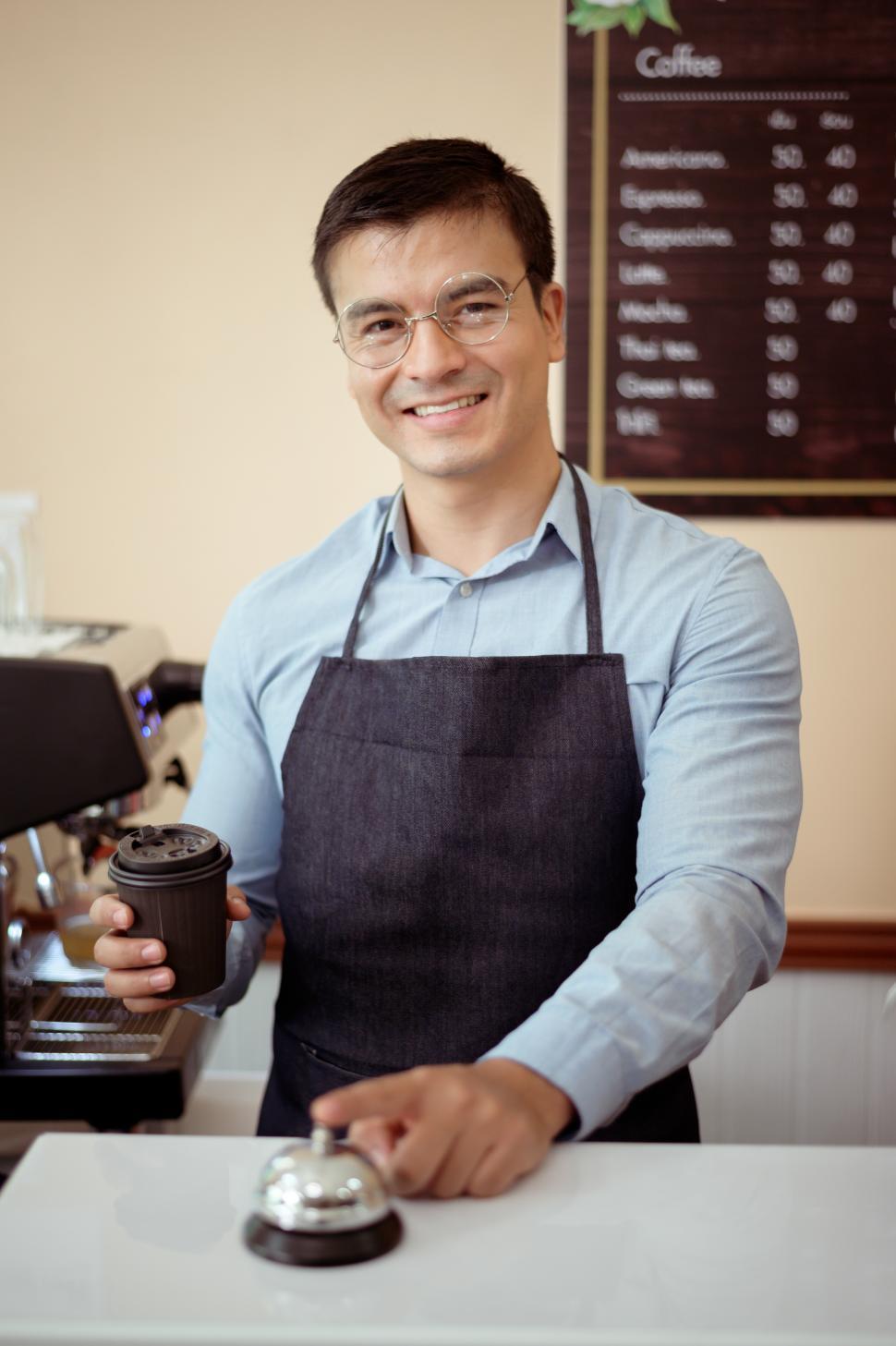 Free Image of Baristas holds a to-go cup full of coffee and has a finger on the service bell 