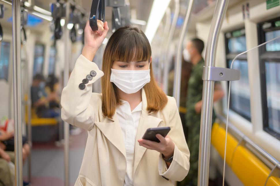 Free Image of Young woman is wearing protective mask in metro looking at her phone 