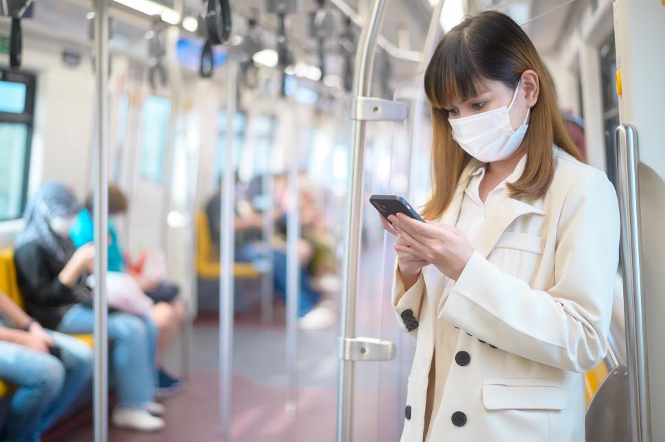 Free Image of Young woman using public transportation, using smartphone, wearing mask 