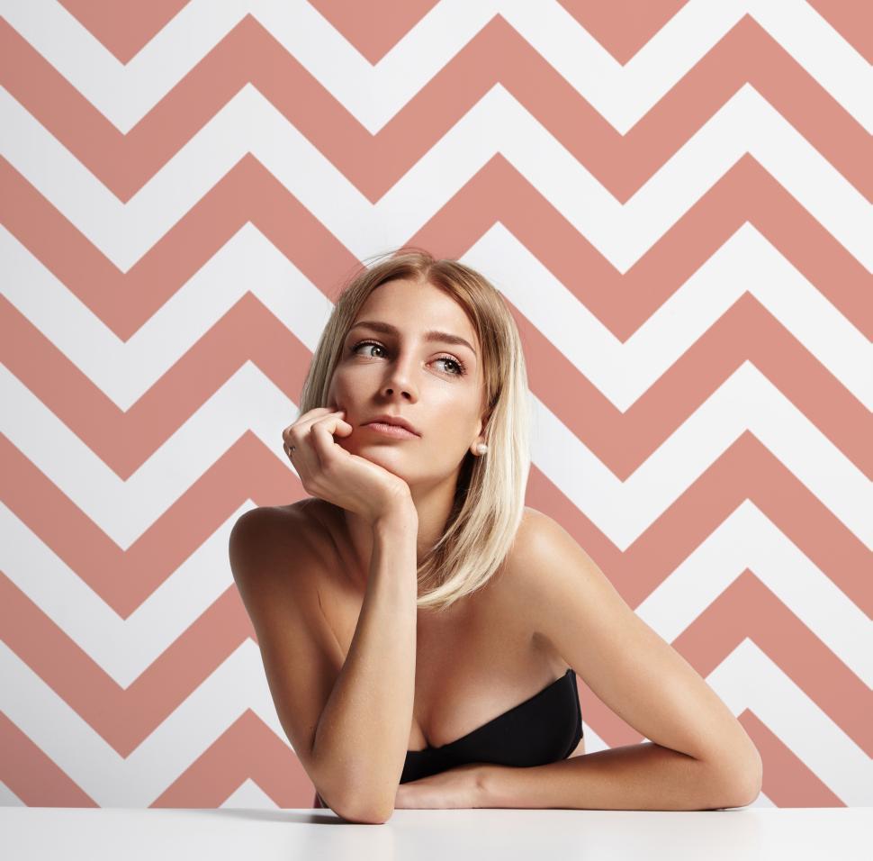 Free Image of woman in a room with trendy printed wall, chin in hand, looking thoughtful 
