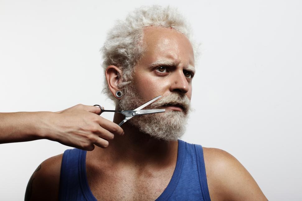 Free Image of Hand with scissors comes from off screen to trim the beard of seated man 
