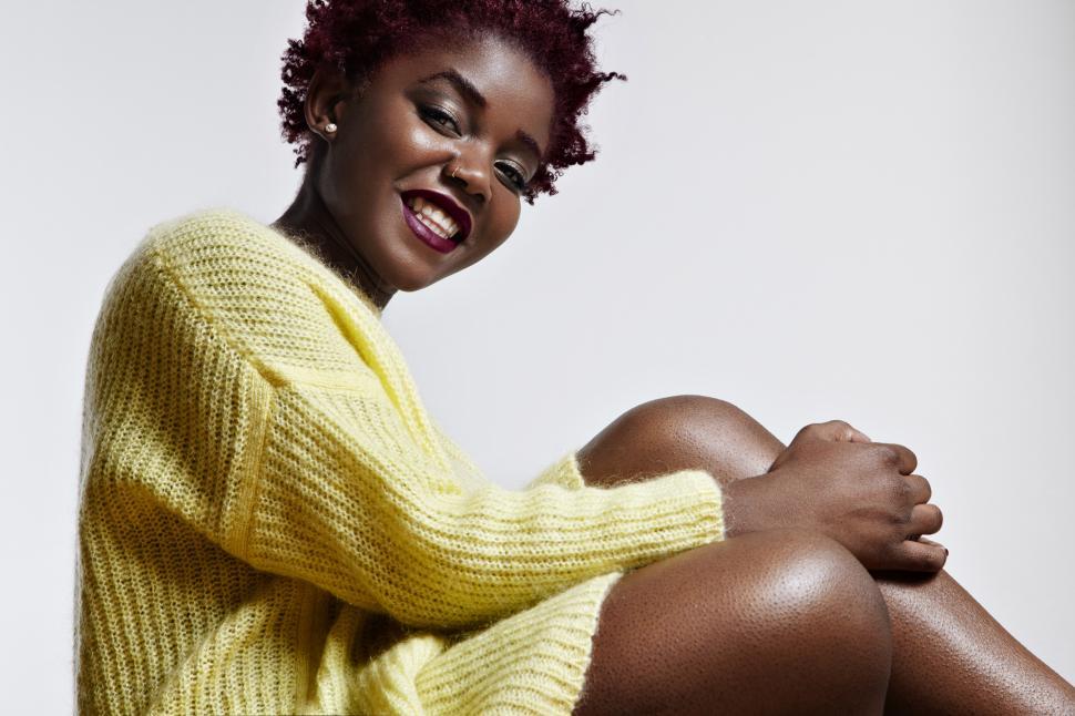 Free Image of Smiling black woman wearing bright sweater, and touching her legs 