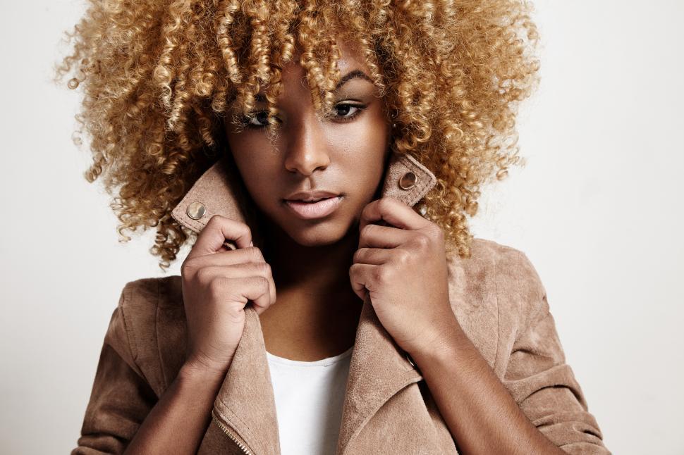 Free Image of black woman wears beige jacket, curly hair, serious look 