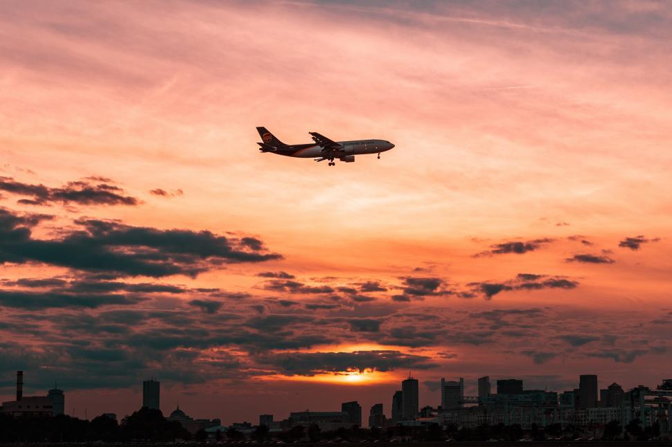 Free Image of Photo of a plane flying over a city at sunset 