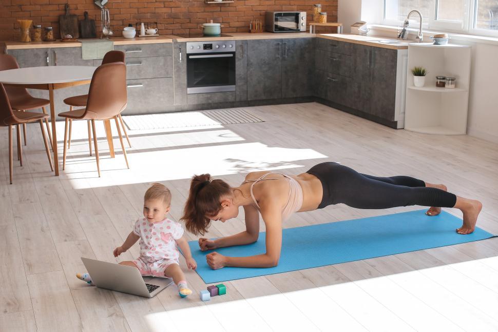 Free Image of A woman doing plank on a mat with a baby on the floor 