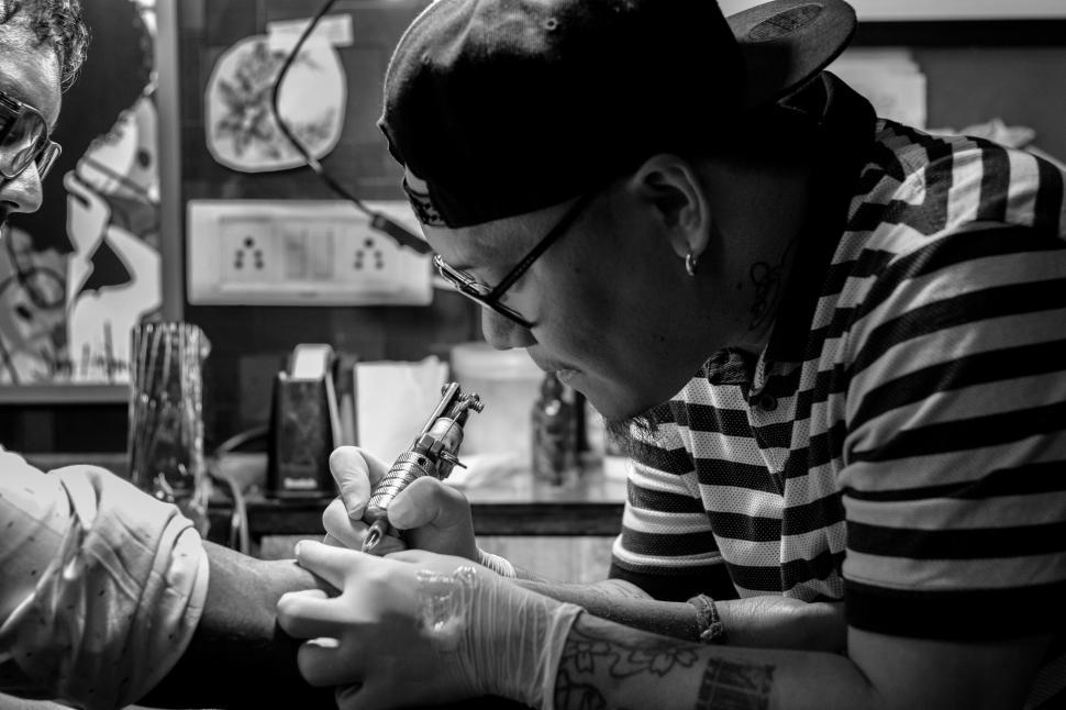 Free Image of A man in a hat tattooing a person s hand 