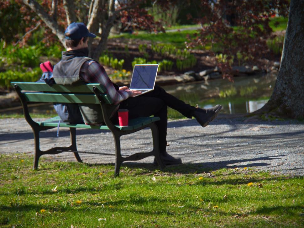 Free Image of A man sitting on a bench with a laptop 