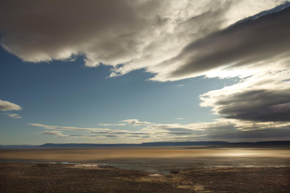 Free Image of A large flat land with a body of water and clouds in the sky 