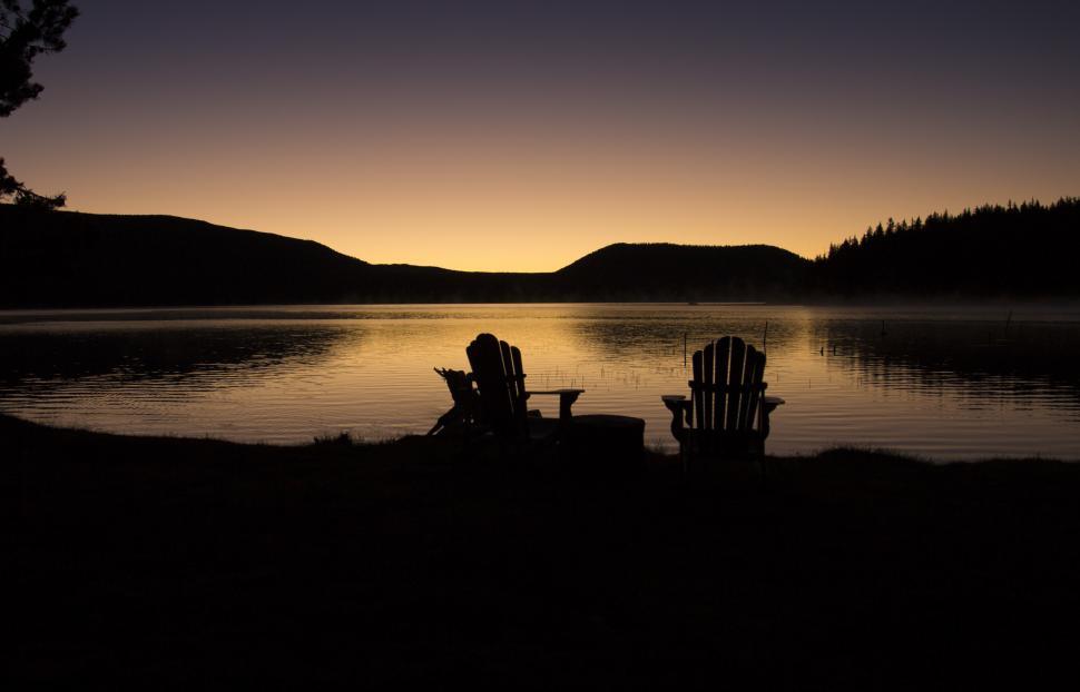 Free Image of A silhouette of chairs and a table by a lake 