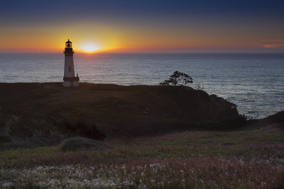 Free Image of A lighthouse on a hill with a sunset in the background 