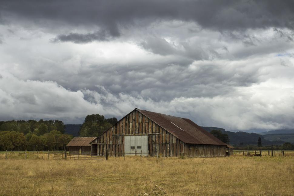 Free Image of A barn in a field with clouds in the sky 