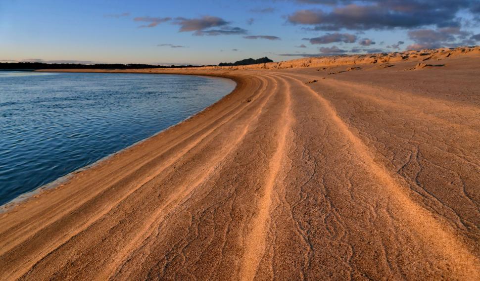 Free Image of A sandy beach with a body of water and blue sky 