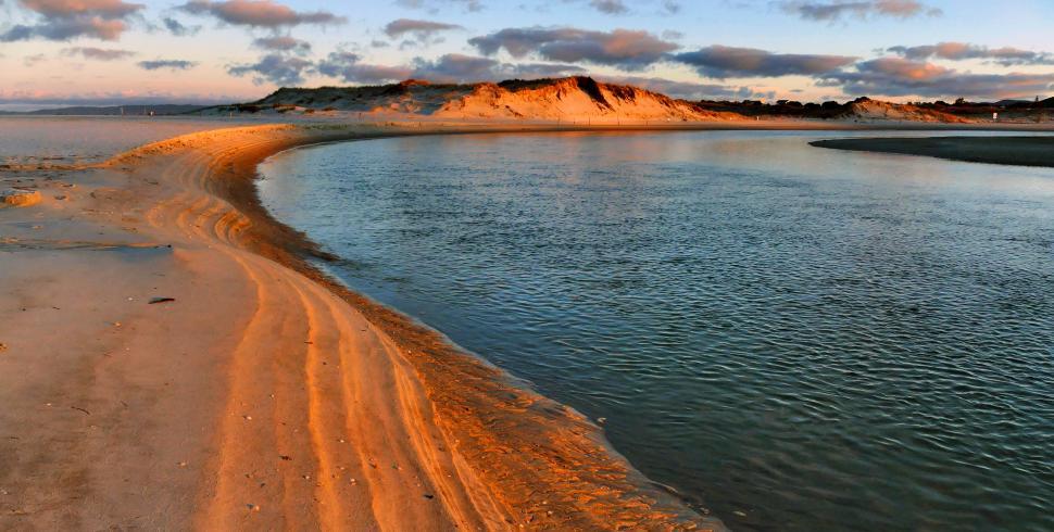 Free Image of A sandy beach with a body of water and hills in the background 