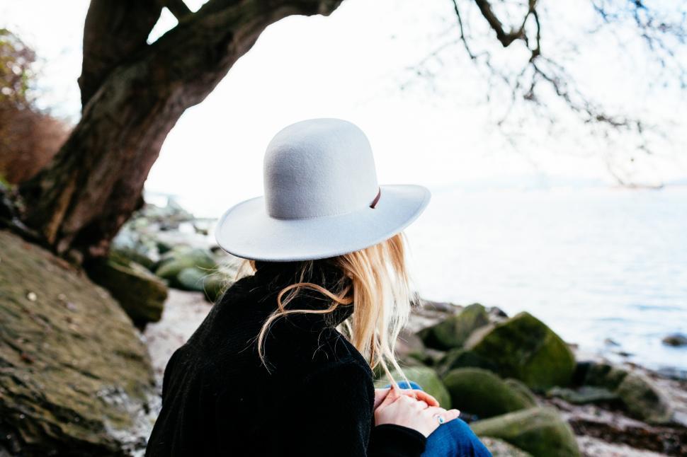 Free Image of A woman wearing a hat and sitting on a rock 