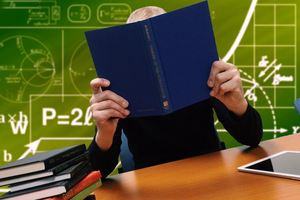 Free Image of A person sitting at a desk with a book in front of their face 