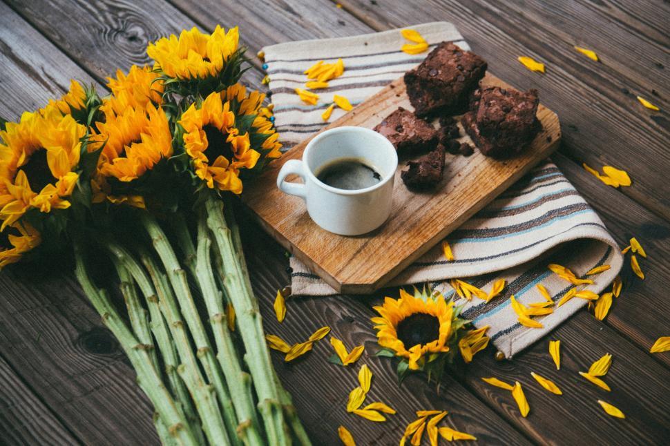 Free Image of A cup of coffee and brownies on a wood board next to yellow flowers 