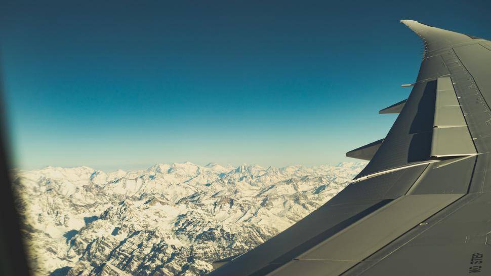 Free Image of A wing of an airplane flying over snowy mountains 