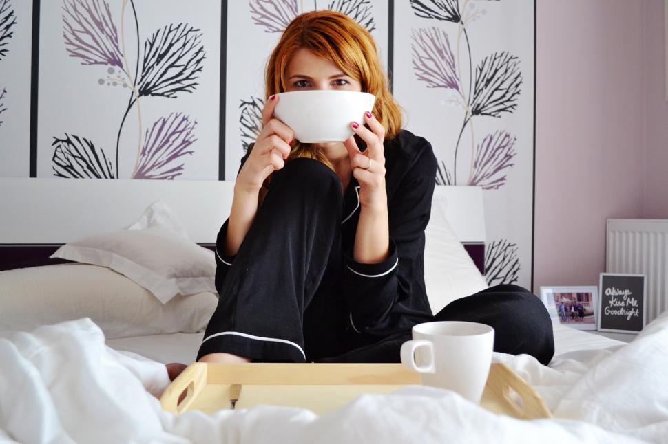 Free Image of A woman sitting on a bed holding a white bowl 