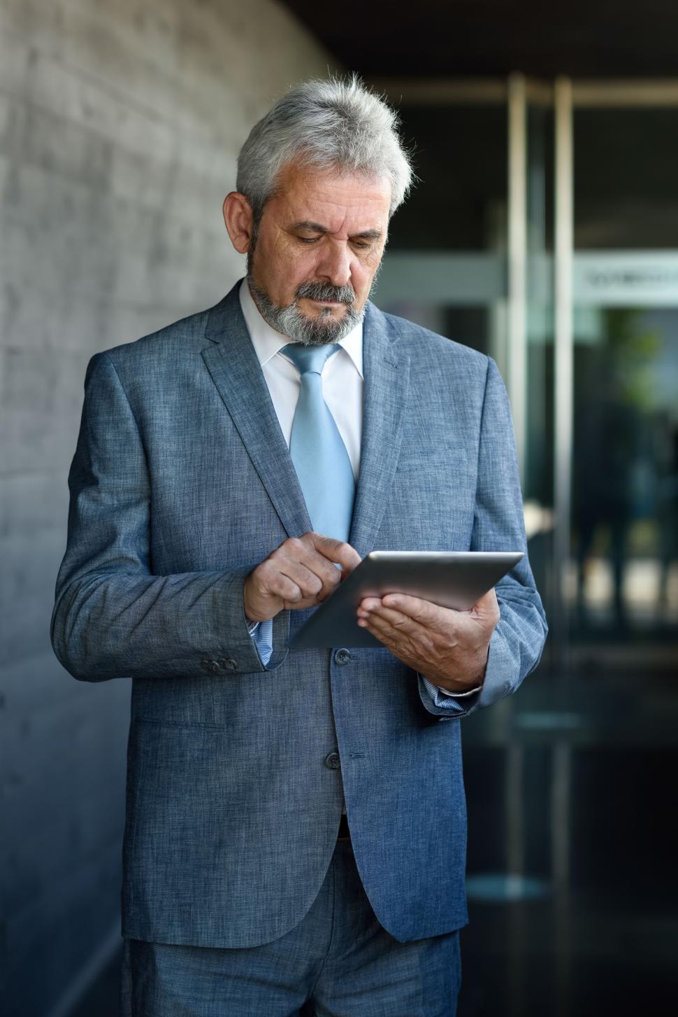 Free Image of Senior businessman with tablet computer outside of modern office building. 