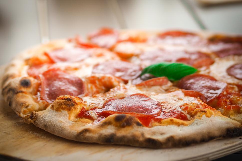 Free Image of A pizza with pepperoni and basil on a wooden surface 