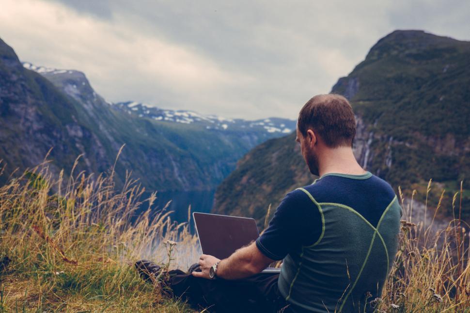 Free Image of A man sitting on grass with a laptop in front of a mountain 