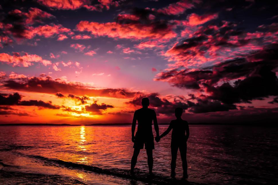 Free Image of Two people holding hands on a beach at sunset 