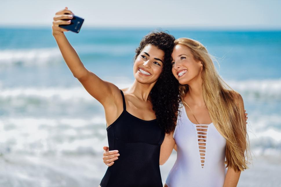 Free Image of Two women taking selfie photograph with smartphone in the beach 