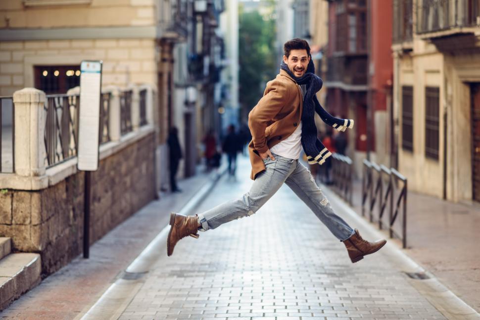 Free Image of Young happy man jumping wearing winter clothes in urban background 