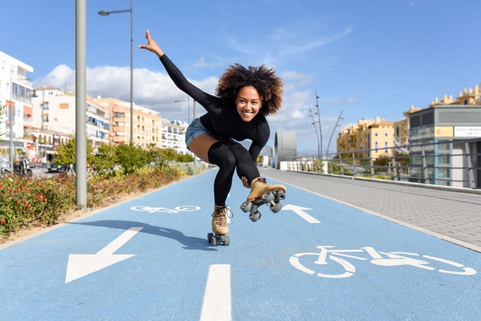 Free Image of Black woman on roller skates riding on bike line 