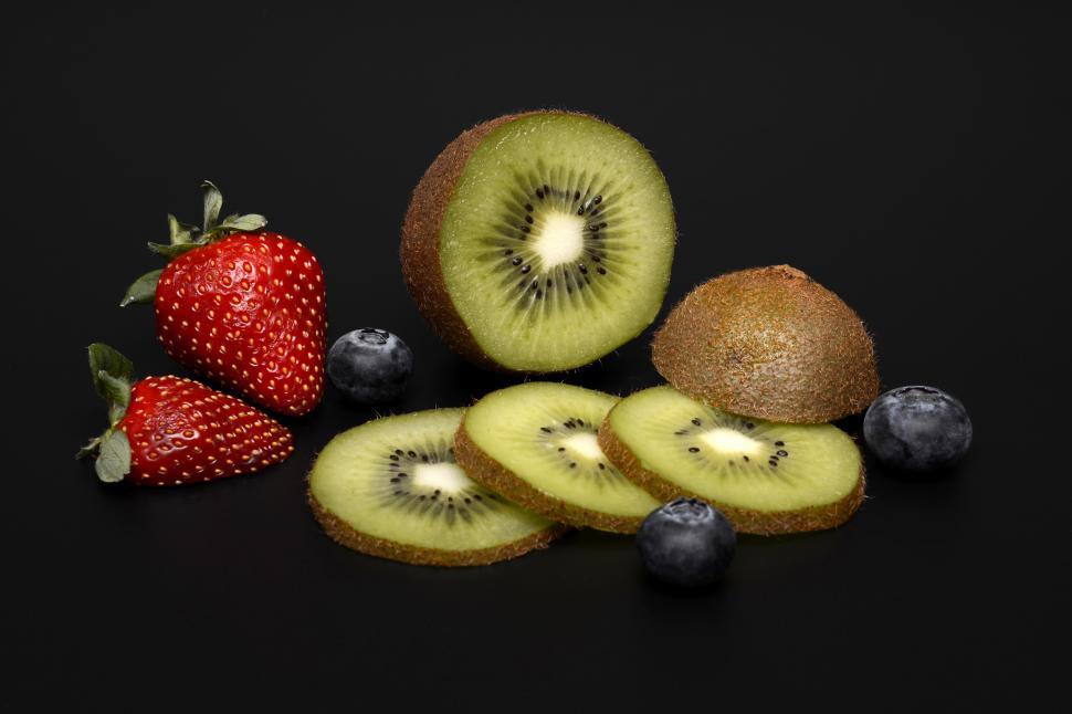 Free Image of A kiwi and strawberries on a black surface 