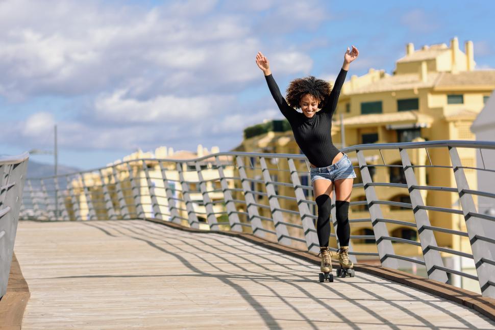 Free Image of Afro hairstyle woman on roller skates riding outdoors on urban bridge 
