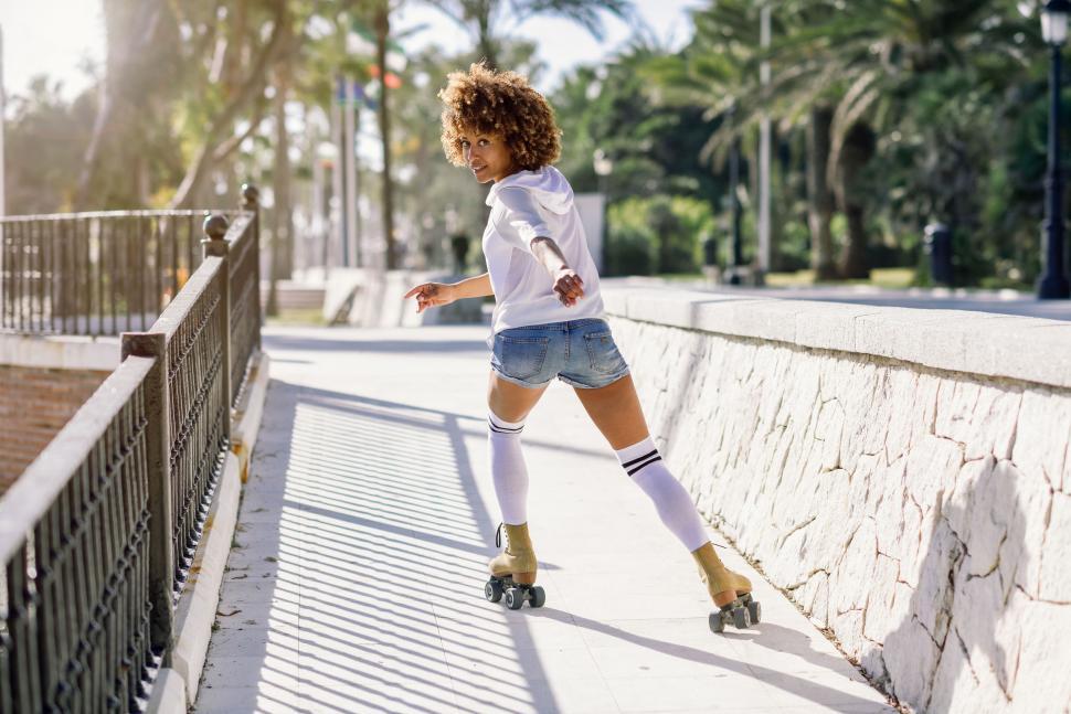 Free Image of Black woman, afro hairstyle, on roller skates riding near the beach. 