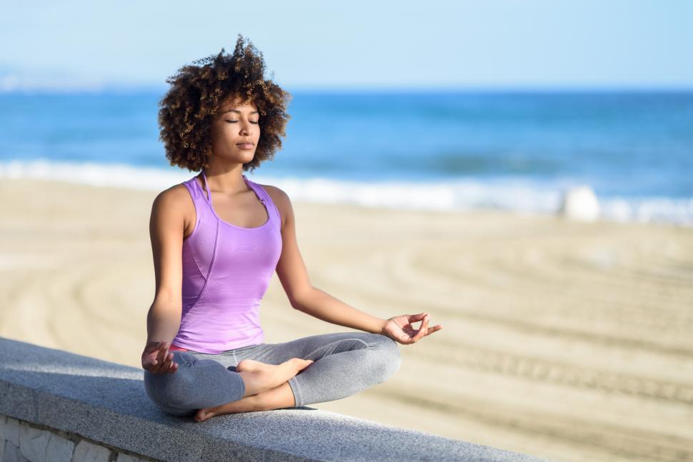 Free Image of Black woman, afro hairstyle, in lotus pose with eyes closed in the beach 