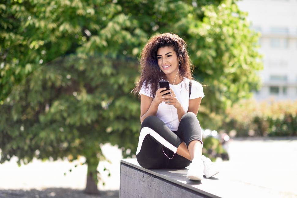 Free Image of Modern Arab woman listening to music with earphones outdoors 