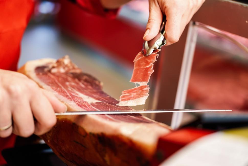 Free Image of Professional cutter carving slices from a whole bone-in serrano ham 
