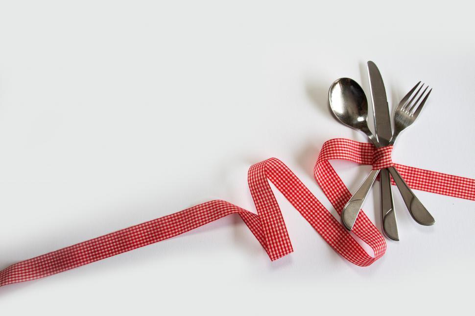 Free Image of A spoons and a red ribbon tied to a white surface 