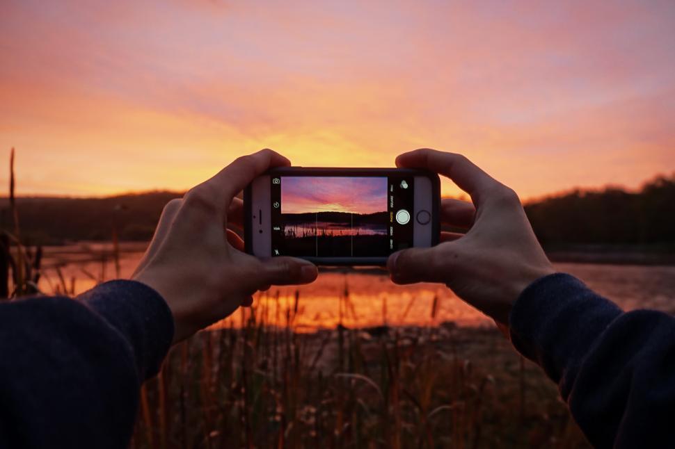 Free Image of A person holding a phone taking a picture of a sunset 