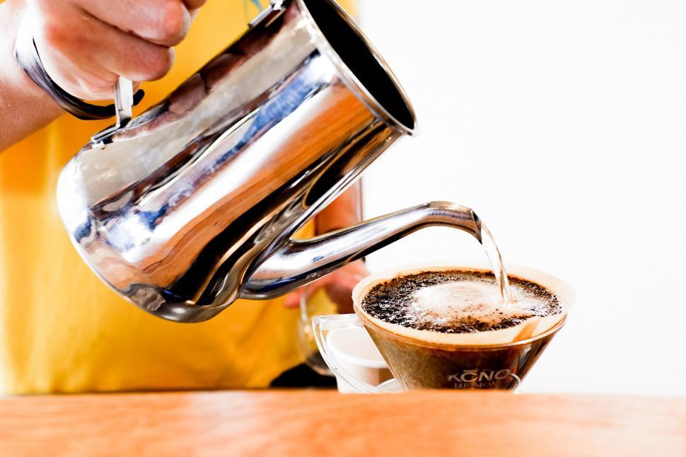 Free Image of A person pouring liquid into a cup of coffee 