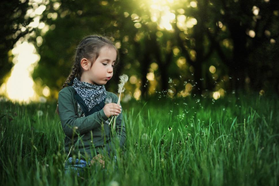 Free Image of A girl blowing dandelion seeds in a grassy field 