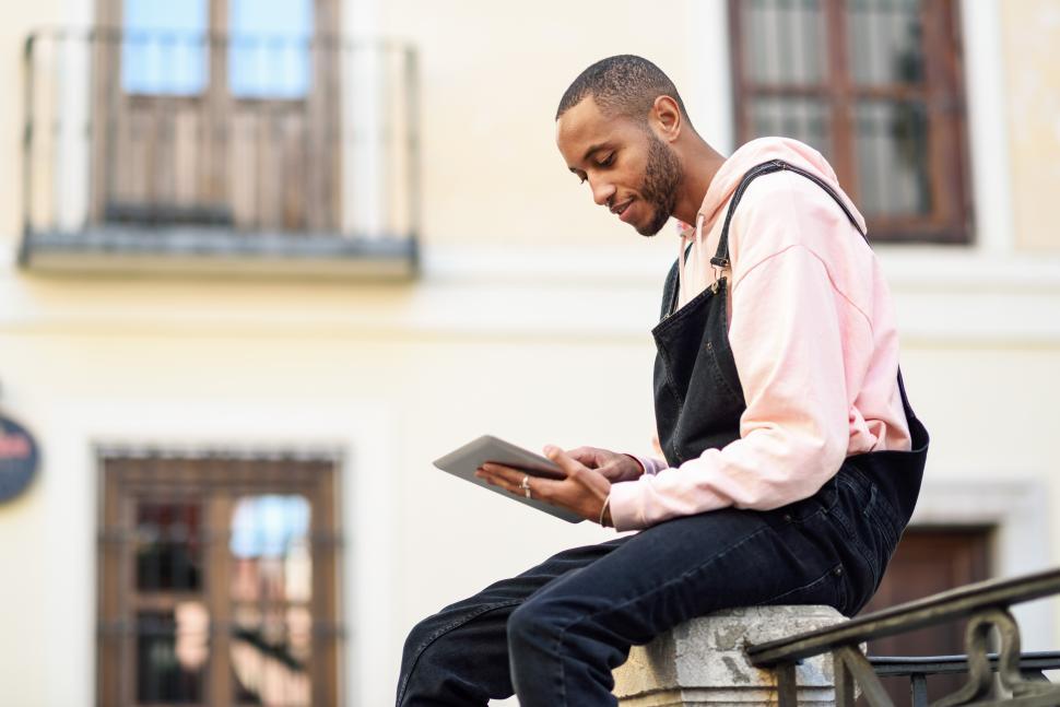 Free Image of Young black man using digital tablet in urban background. 