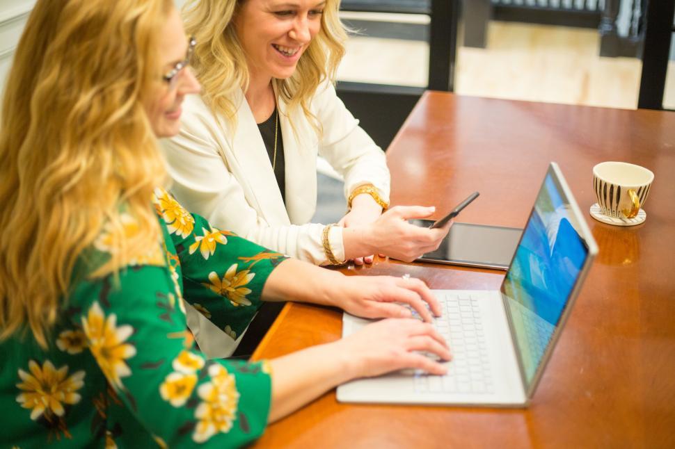 Free Image of A couple of women sitting at a table looking at a laptop 