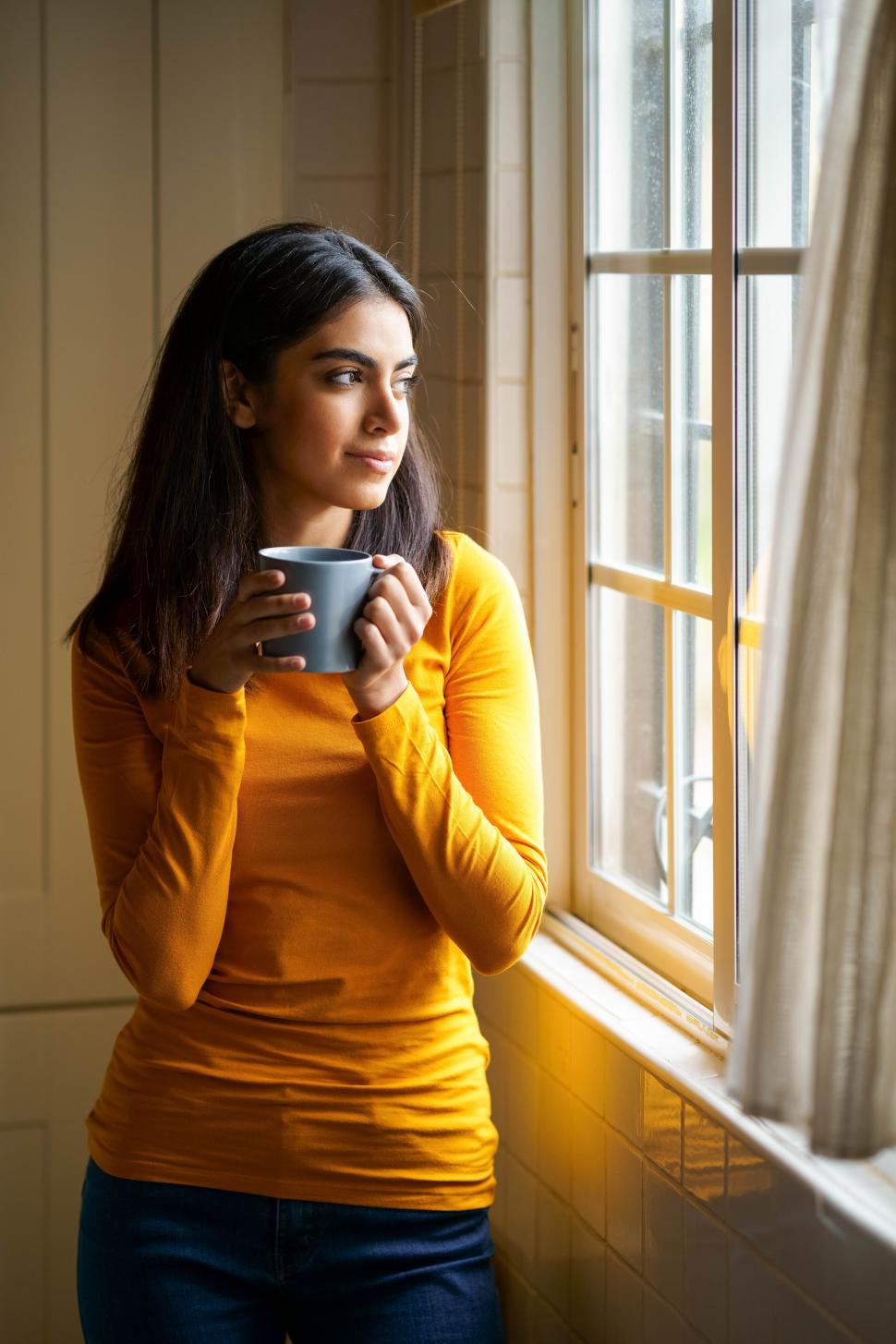Free Image of Persian woman drinking coffee while looking through the window 