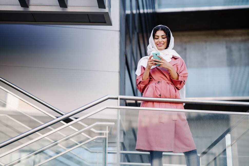 Free Image of Young Muslim woman wearing hijab texting message with her smartphone. 