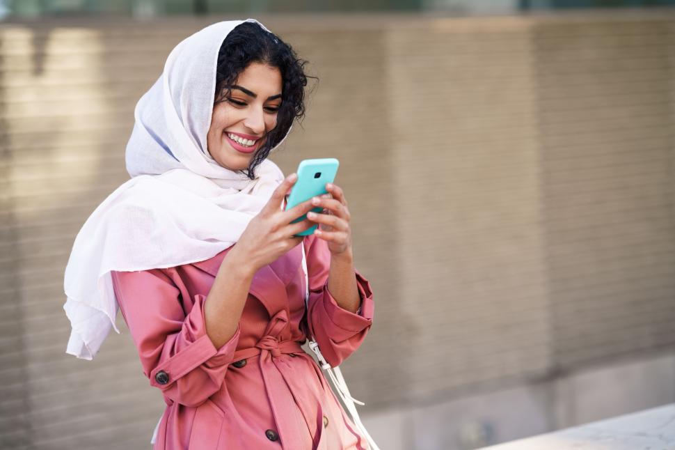 Free Image of Young Arab woman wearing hijab texting message with her smartphone. 