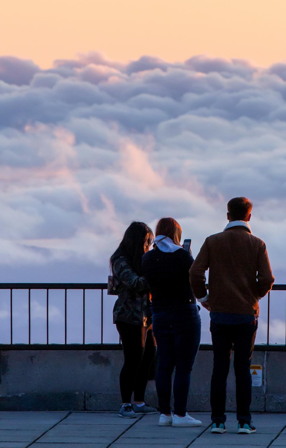 Free Image of A group of people standing on a balcony overlooking clouds 